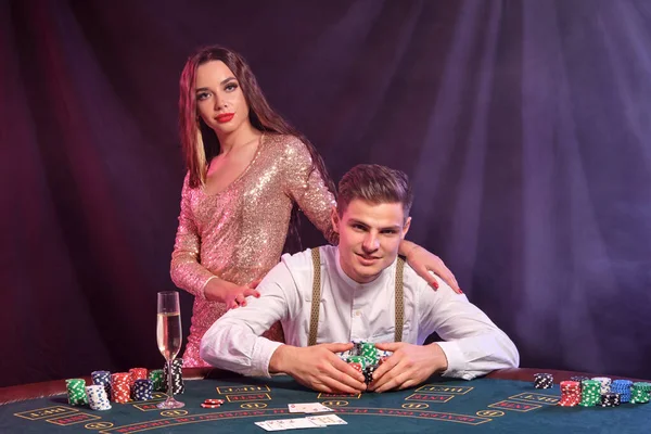 Hombre jugando al póquer en el casino, sentado en la mesa con montones de fichas y cartas en él. Celebrar la victoria con la mujer. Fondos negros de humo. Cierre. — Foto de Stock