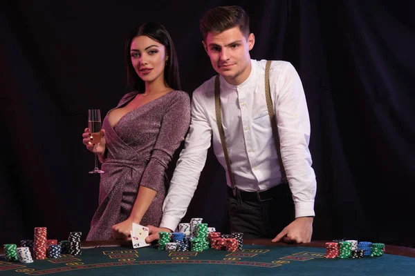 Guy in white shirt está jugando al póquer en el casino, en la mesa con montones de fichas en él. Él celebra la victoria con sexy hembra. Fondos negros. Cierre. — Foto de Stock