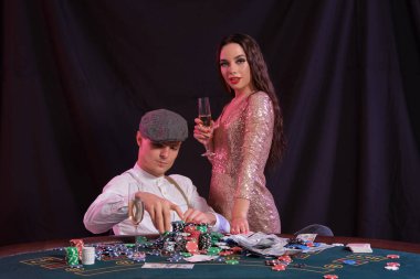 Kumarhanede poker oynayan bir adam masasında yığınla fiş, para, şampanya ve kartlarla oturuyor. Kadınlarla kazanmayı kutluyoruz. Siyah arka plan. Yakın plan..