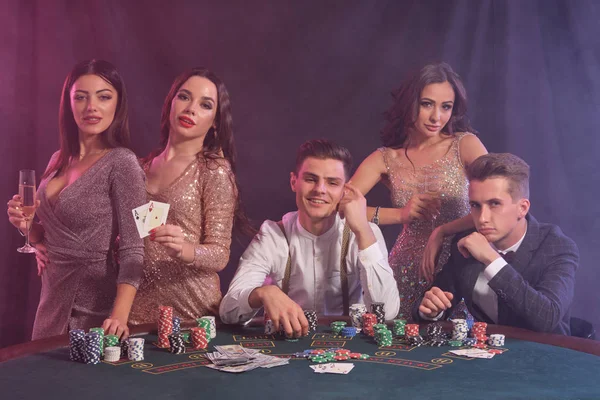 Φίλοι που παίζουν πόκερ στο καζίνο, στο τραπέζι με στοίβες από μάρκες, χρήματα, κάρτες. Γιορτάζουμε τη νίκη, χαμογελάμε. Μαύρο, φόντο καπνού. Κοντινό πλάνο. — Φωτογραφία Αρχείου