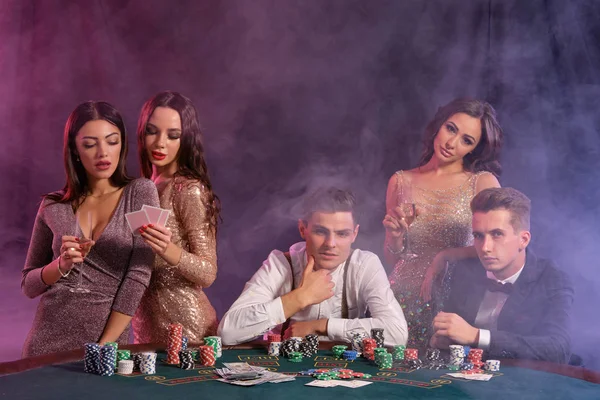Freunde spielen Poker im Casino, am Tisch mit Stapeln von Chips, Geld, Karten darauf. Sieg feiern, lächeln. Schwarzer, rauchiger Hintergrund. Nahaufnahme. — Stockfoto