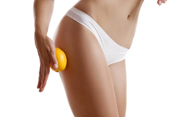 Perfektní tělo dívky v bílém spodním prádle, dotýkající se jejího boku citrónem, izolované na bílém. Plastická chirurgie a estetická kosmetologie. Detailní záběr. — Stock fotografie