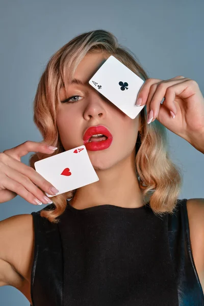 Blond flicka i svart läder klänning visar två spelkort, poserar mot grå bakgrund. Spelunderhållning, poker, kasino. Närbild. — Stockfoto