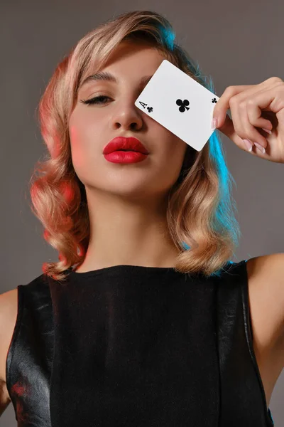 Nieta rubia vestida de cuero negro mostrando la cara de los clubes, posando sobre fondo gris. Juegos de entretenimiento, póquer, casino. Cierre. — Foto de Stock