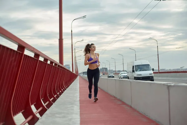 Kız sporcu kız sabahları dışarıda, şehirde modern köprü nehrinde koşuyor. Aktif sağlıklı yaşam tarzı. Spor ve eğlence konsepti. — Stok fotoğraf