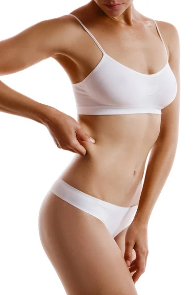 Ung kropp av flicka i vita underkläder, visar fett på sin sida, poserar isolerad på vitt. Plastikkirurgi, estetisk kosmetologi koncept. Närbild. — Stockfoto