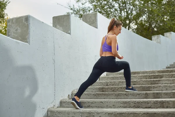 Kız sporcu kız sabahları dışarıda, şehirde yeşil ağaçlarla çevrili merdivenlerde geriniyor. Aktif sağlıklı yaşam tarzı. Spor ve eğlence konsepti. — Stok fotoğraf