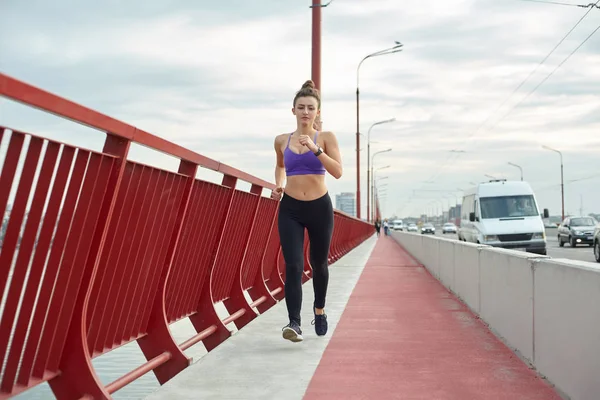 Atleta menina está correndo pela manhã fora, na cidade, na ponte moderna que cruza o rio. Estilo de vida saudável ativo. Conceito de esporte e recreação. — Fotografia de Stock