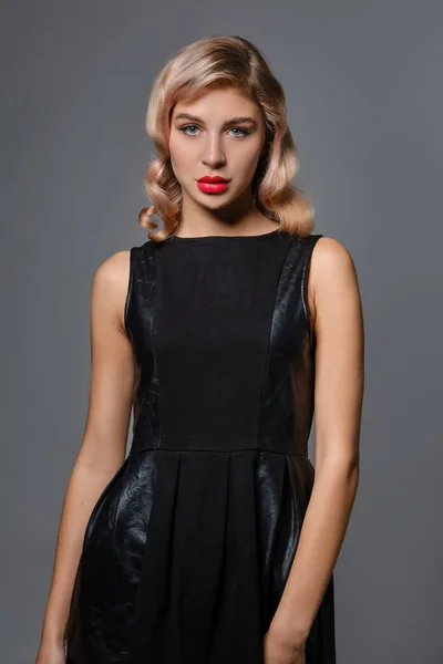 Beautiful blonde girl with bright make-up, in black short leather dress is posing against gray studio background. Fashion and beauty. Close-up. – stockfoto