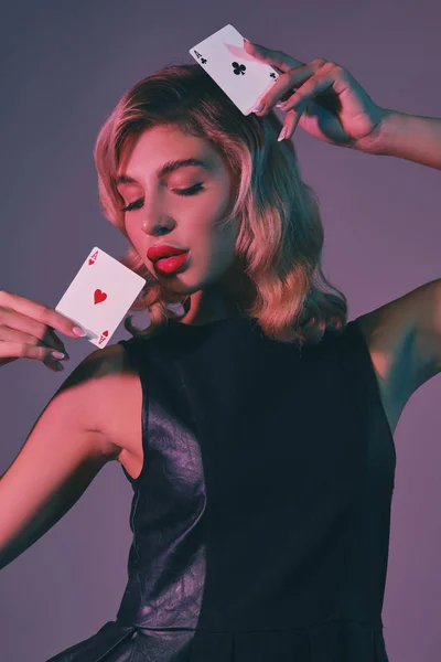 Szőke lány fekete elegáns ruha mutatja két kártya, pózol a színes háttér. Szerencsejáték, póker, kaszinó. Közelkép. — Stock Fotó