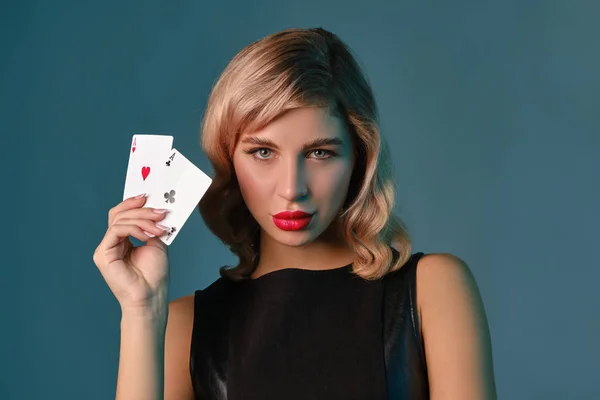 Chica rubia en vestido elegante negro que muestra dos cartas de juego, posando sobre fondo azul. Entretenimiento, póquer, casino. Primer plano . — Foto de Stock