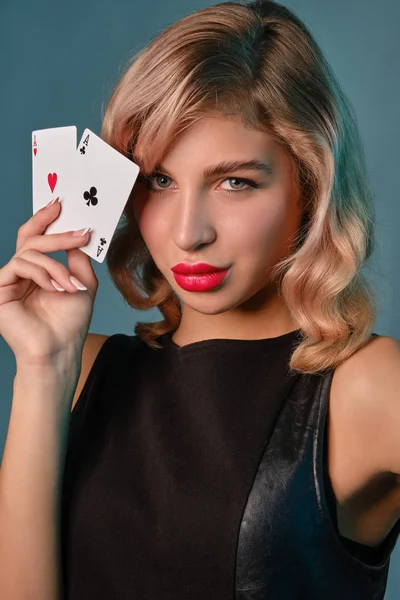 Blond flicka i svart elegant klänning visar två spelkort, poserar mot blå bakgrund. Spelunderhållning, poker, kasino. Närbild. — Stockfoto