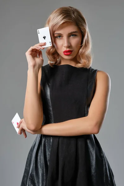 Блондинка в черном стильном платье показывает две игральные карты, позируя на сером фоне. Азартные игры, покер, казино. Крупный план . — стоковое фото