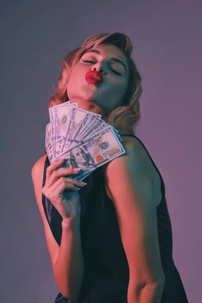 Блондинка в черном стильном платье, держащая в руках деньги, позирует на цветном фоне. Азартные игры, покер, казино. Закрытие. — стоковое фото