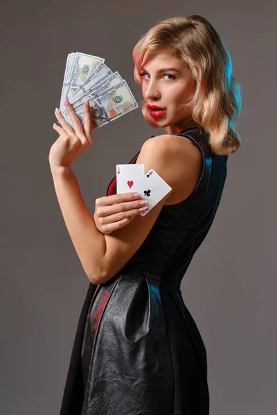 黒のスタイリッシュなドレスのブロンドの女の子は、灰色の背景に対してポーズをいくつかのお金とカードを保持。ギャンブルエンターテイメント,ポーカー,カジノ.閉鎖. — ストック写真