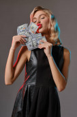 Blondýny dívka v černém stylové šaty držení a líbání nějaké peníze, pózování na šedém pozadí. Hazardní hry, poker, kasino. Detailní záběr.
