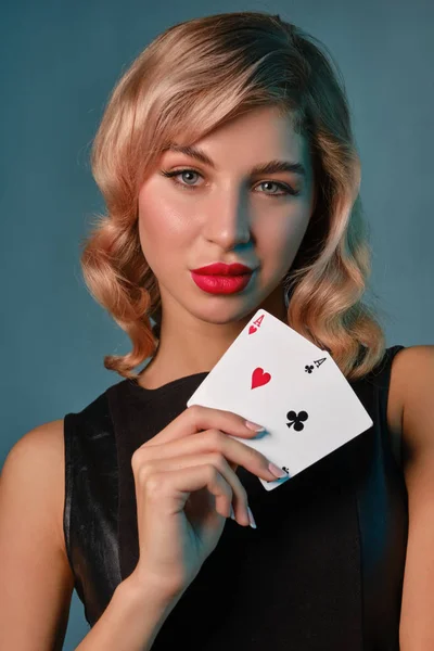 Chica rubia en vestido elegante negro que muestra dos cartas de juego, posando sobre fondo azul. Entretenimiento, póquer, casino. Primer plano . — Foto de Stock