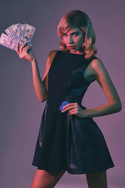 Блондинка в черном стильном платье держит деньги и чипсы, позируя на красочном фоне. Азартные игры, покер, казино. Крупный план . — стоковое фото