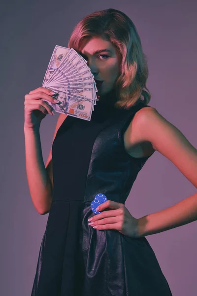 Блондинка в черном стильном платье держит деньги и чипсы, позируя на красочном фоне. Азартные игры, покер, казино. Крупный план . — стоковое фото