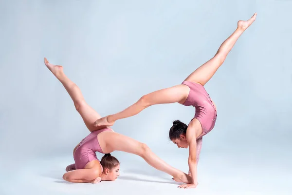 Two flexible girls gymnasts in pink leotards are doing exercises using support and posing isolated on white background. Close-up.