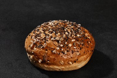 Taze, lezzetli pişmiş çörek üzerine susam ve ayçekirdeği serpiştirilmiş siyah arka planda fotokopi alanı ile. Kırsal mutfak ya da fırın. Yakın plan.