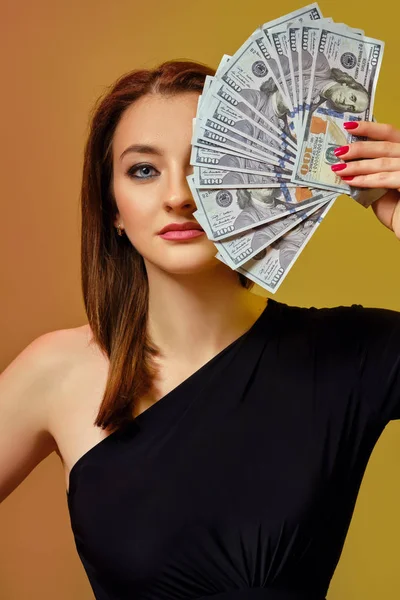 Blonďatá modelka v černých šatech si zakryla půlku obličeje nějakou hotovostí, pózuje na barevném pozadí. Poker, kasino. Detailní záběr. — Stock fotografie