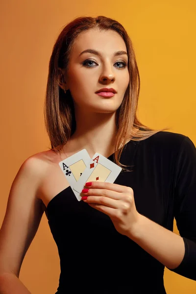 Blond modell med ljusa make-up, i svart klänning visar två ess, poserar mot färgglada bakgrund. Spel, poker, kasino. Närbild. — Stockfoto