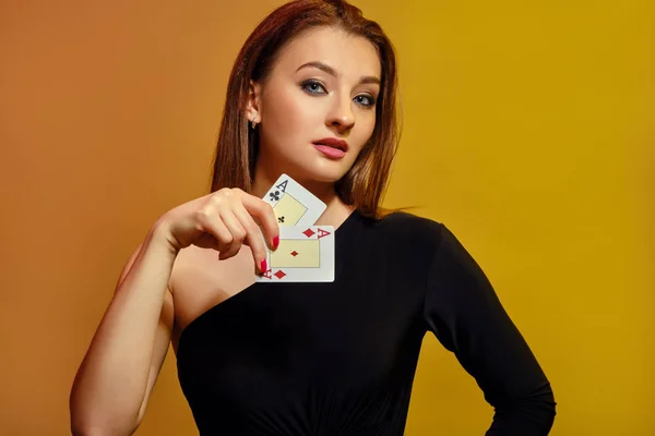 Blonďatá fenka s jasným make-upem, v černých šatech ukazuje dvě esa, pózující na barevném pozadí. Hazard, poker, kasino. Detailní záběr. — Stock fotografie