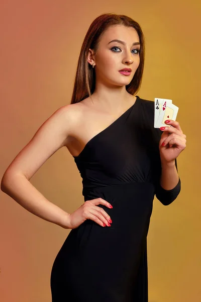 Blonďatá žena s jasným make-upem, v černých šatech ukazuje dvě esa, pózující na barevném pozadí. Hazard, poker, kasino. Detailní záběr. — Stock fotografie