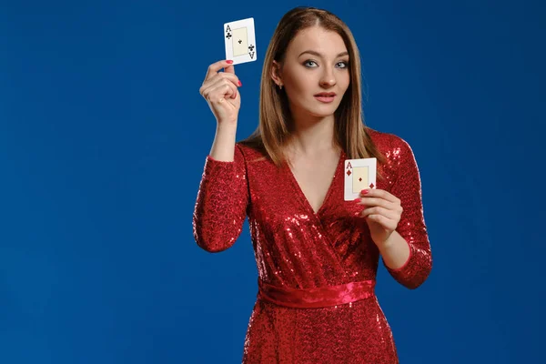 Fille blonde avec maquillage, en robe à paillettes rouges montre deux as, posant sur fond bleu. Jeux d'argent, poker, casino. Gros plan . — Photo