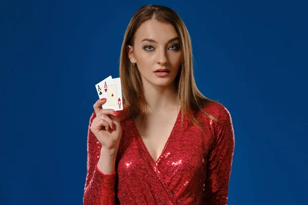 Donna bionda con il trucco, in abito rosso di paillettes sta mostrando due assi, in posa su sfondo blu. Gioco d'azzardo, poker, casinò. Primo piano . — Foto Stock