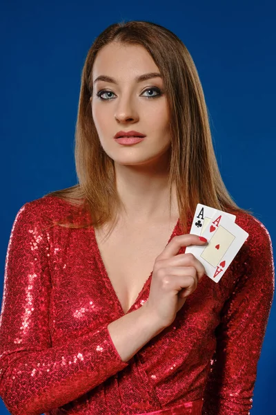 Blonďatá žena s make-upem, v červených flitrových šatech ukazuje dvě esa, pózující na modrém pozadí. Hazard, poker, kasino. Detailní záběr. — Stock fotografie