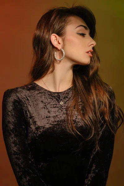 Vonzó barna nő elegáns ékszerek és fekete bársony ruha, pózol ellen színes háttér. Divat és szépség. Közelkép, fénymásolás — Stock Fotó