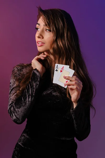 Donna bruna in abito di velluto nero che mostra due carte da gioco, in posa su sfondo colorato. Intrattenimento di gioco, poker, casino '. Primo piano . — Foto Stock
