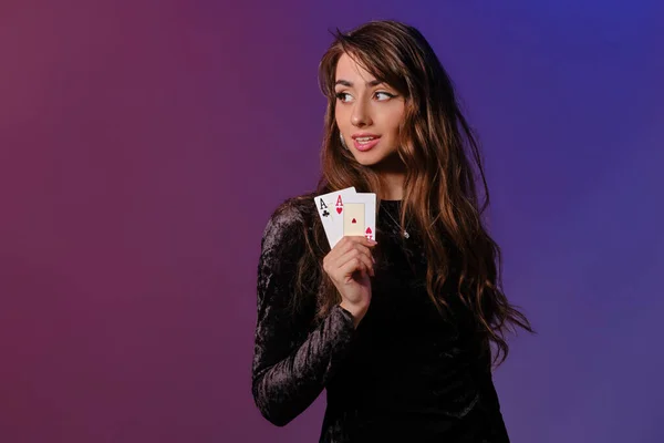 Donna bruna in abito di velluto nero che mostra due carte da gioco, in posa su sfondo colorato. Intrattenimento di gioco, poker, casino '. Primo piano . — Foto Stock