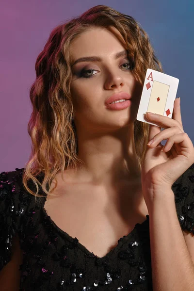 Donna dai capelli castani in abito nero lucido mostrando asso di diamanti, in posa su sfondo colorato. Intrattenimento di gioco, poker, casino '. Primo piano . — Foto Stock