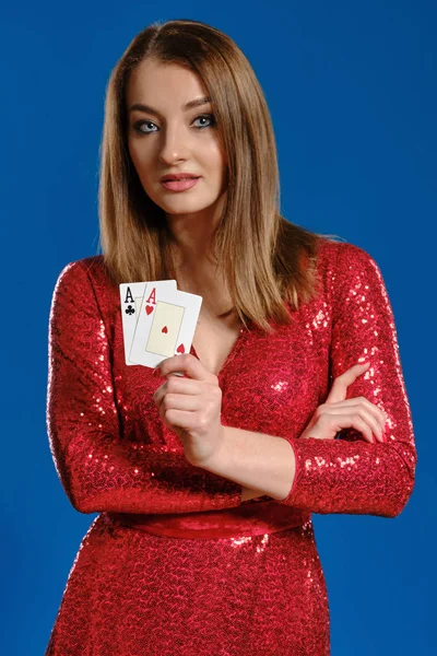Donna bionda con il trucco, in abito di paillettes rosso mostra due assi, le mani incrociate, in posa su sfondo blu. Gioco d'azzardo, poker, casinò. Primo piano . — Foto Stock