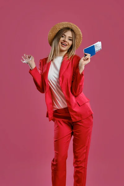 밀짚모자에 흰 블라우스에 빨간 팬츠를 입은 금발 소녀. 그녀는 분홍색 스튜디오 배경에 대해 포즈를 취하면서 여권 과 티켓을 들고 있다. 클로즈업 — 스톡 사진