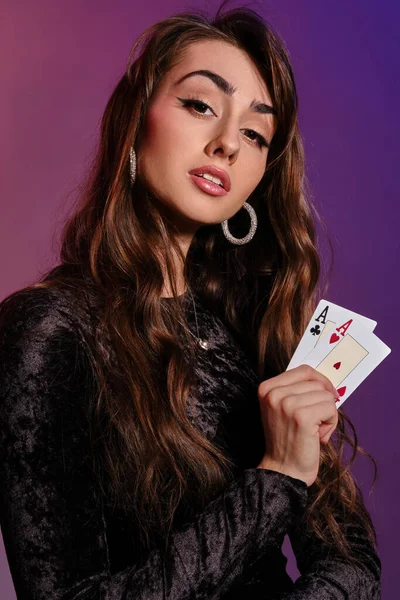 Mulher morena em vestido de veludo preto mostrando duas cartas de jogo, posando contra fundo colorido. Entretenimento de jogo, póquer, casino. Close-up . — Fotografia de Stock