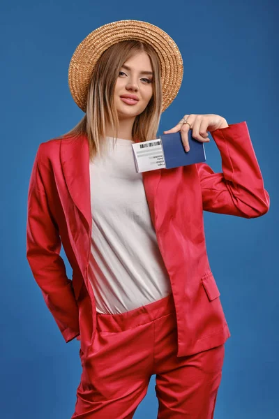 밀짚모자에 흰 블라우스에 빨간 팬츠 정장을 입은 금발 모델. 그녀는 웃으며 파란 스튜디오 배경에 포즈를 취하면서 여권 과 티켓을 보여 줬다. 클로즈업 — 스톡 사진