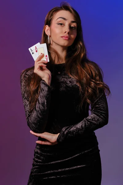 Mujer morena en vestido de terciopelo negro mostrando dos cartas de juego, posando sobre fondo coloful. Entretenimiento, póquer, casino. Primer plano . —  Fotos de Stock