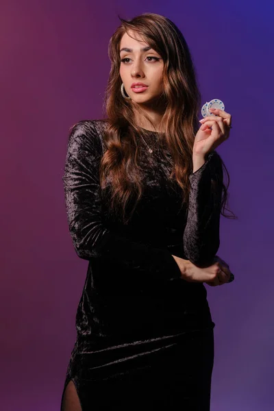 Brunette woman in black velvet dress showing multicolored chips, posing against coloful background. Gambling entertainment, poker, casino. Close-up. — Stock Photo, Image