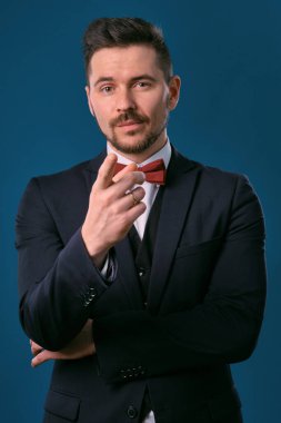 Young business man in classic black suit, white shirt and red bow-tie. Posing against a blue studio background. Mock up, copy space. Close-up.