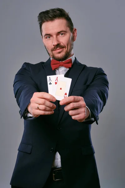 Man in black classic suit and red bow-tie showing two playing cards while posing against gray studio background. Gambling, poker, casino. Close-up. — Φωτογραφία Αρχείου