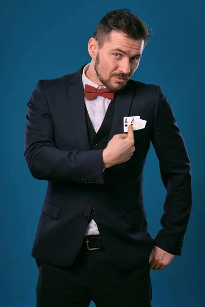 Чоловік в чорному класичному костюмі і червона краватка з двома гральними картами, позуючи на синьому студійному фоні. Азартні ігри, покер, казино. Крупним планом . — стокове фото