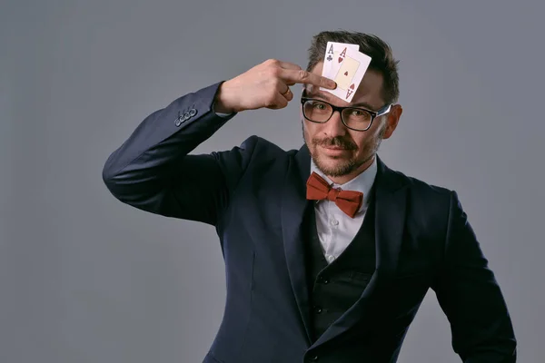 Чоловік в чорному класичному костюмі, червона краватка, гладес показує дві ігрові картки, позує на сірому студійному фоні. Азартні ігри, покер, казино. Крупним планом . — стокове фото