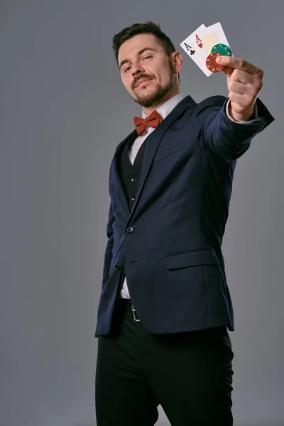 Чоловік в чорному класичному костюмі і червона краватка з двома гральними картками і фішками, позує на сірому студійному фоні. Азартні ігри, покер, казино. Крупним планом . — стокове фото