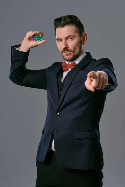 Чоловік в чорному класичному костюмі і червона краватка, що показує деякі кольорові чіпси, позує на сірому студійному фоні. Азартні ігри, покер, казино. Крупним планом . — стокове фото