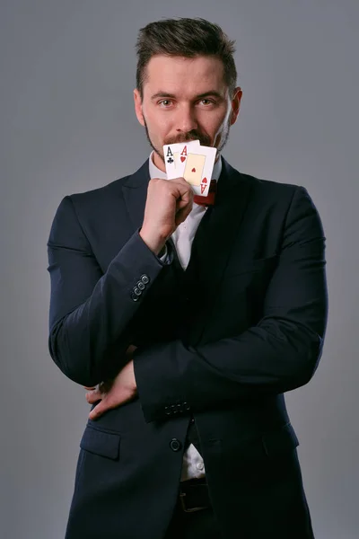 Чоловік в чорному класичному костюмі і червона краватка з двома гральними картами, позуючи на сірому студійному фоні. Азартні ігри, покер, казино. Крупним планом . — стокове фото