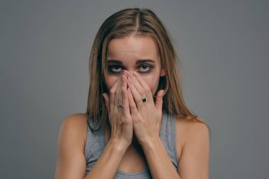 Yüzünde morluklar olan sarışın kız gri arka planda poz veriyor. Aile içi şiddet, taciz. Depresyon, umutsuzluk. Yakın plan, kopyalama alanı.